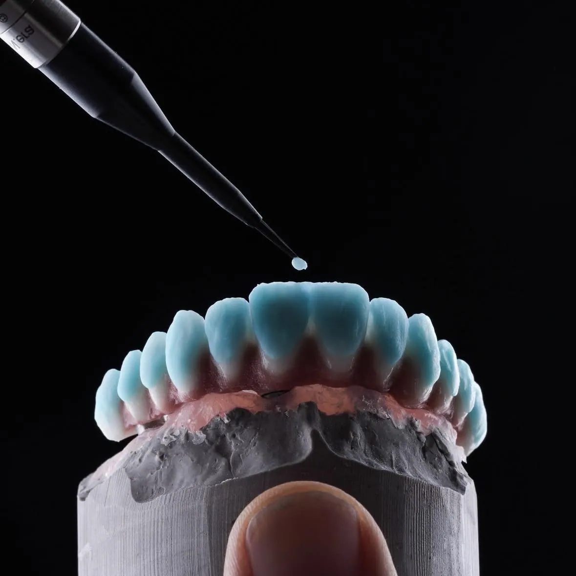Porcelain being applied by hand to a full-arch bridge, with pink porcelain at the gum line